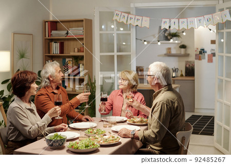 Group of senior friends with glasses of wine congratulating happy aged woman 92485267