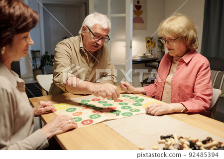 Senior man moving chip throughout paper board with green and red circles 92485394
