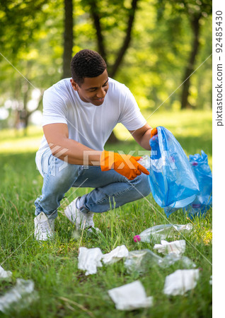 Man in gloves picking up trash in forest 92485430