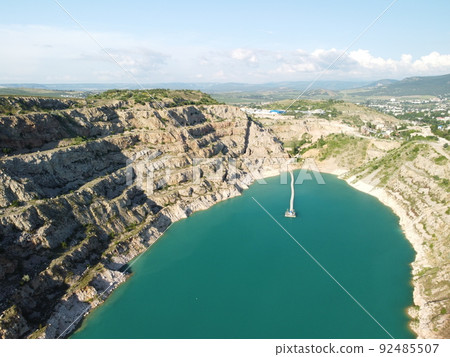 Aerial top view on opencast mining quarry with flooded bottom, turquoise surface of the lake. Quarry pond overgrown with green plants and clear turquoise water Aerial top view on opencast mining quarry with flooded bottom, turquoise surface of the lake. Quarry pond overgrown with green plants and clear turquoise water 92485507
