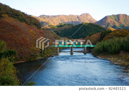 Daigo-cho, a train that crosses the iron bridge of the Kuji River against the backdrop of the mountains of autumn leaves 92485521