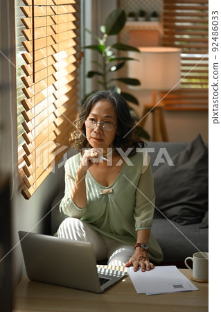 Middle aged woman resting on couch and looking through the window, enjoy stress free peaceful mood at home Middle aged woman resting on couch and looking through the window, enjoy stress free peaceful mood at home 92486033