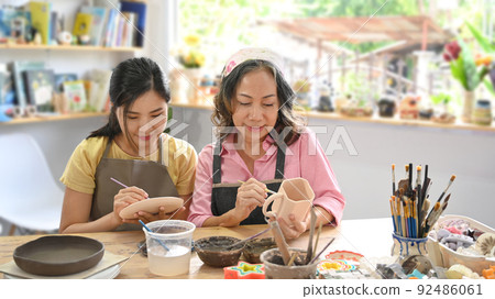 Young woman and retired woman painting painting on bowl before baking in pottery workshop 92486061