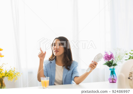A woman seeking coolness with an electric fan 92486997