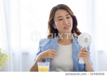 A woman seeking coolness with an electric fan 92486998