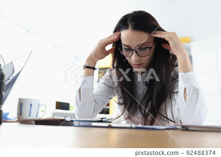 Tired sleepy woman sits at table holds head and rests at the workplace 92488374