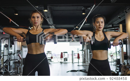 Two  sporty girls do exercises with dumbbells in  the gym. 92488458