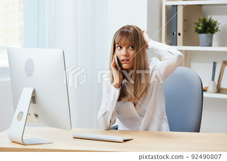 Excited adorable blonde businesswoman worker make difficult decision talking with client in call in light modern office. Nervous employee work on computer online in support service. Copy space 92490807