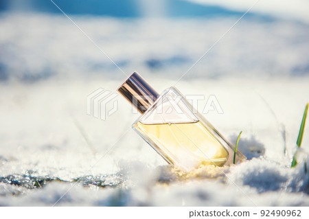 A rectangular transparent glass bottle of golden perfume stands in snow. Blurred background. Concept of template of perfumes and fragrance A rectangular transparent glass bottle of golden perfume stands in snow. Blurred background. Concept of template of perfumes and fragrance 92490962