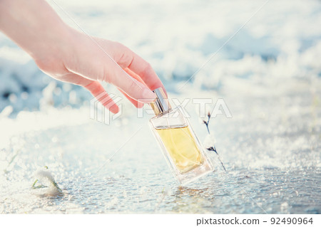 A woman's hand gracefully holds a rectangular transparent glass bottle of golden perfume on ice. Blurred background. Perfume and Fragrance template concept A woman's hand gracefully holds a rectangular transparent glass bottle of golden perfume on ice. Blurred background. Perfume and Fragrance template concept 92490964