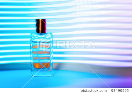 Transparent perfume rectangular bottle on striped blue background, neon light. Copy space. Fashionable Perfume template Transparent perfume rectangular bottle on striped blue background, neon light. Copy space. Fashionable Perfume template 92490965