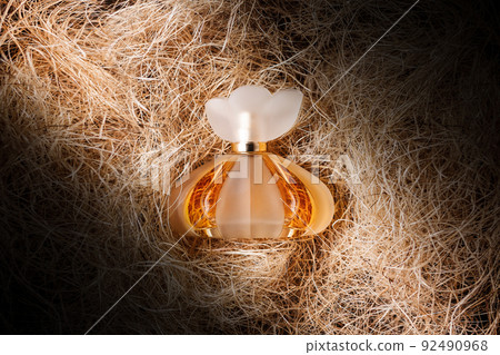 A transparent bottle of golden perfume on the hay. Flat lay. Light beam. The concept of beauty industry and perfumery A transparent bottle of golden perfume on the hay. Flat lay. Light beam. The concept of beauty industry and perfumery 92490968
