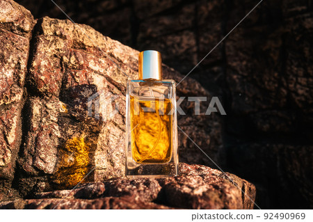 A glass rectangular bottle of golden perfume standing on a stone. Copy space A glass rectangular bottle of golden perfume standing on a stone. Copy space 92490969