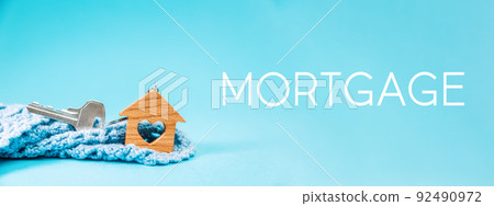 Web banner of mortgage. Close-up of a key and small keychain wooden house with a heart lying in a knitted scarf. Blue background. The concept of leasing and home purchase Web banner of mortgage. Close-up of a key and small keychain wooden house with a heart lying in a knitted scarf. Blue background. The concept of leasing and home purchase 92490972