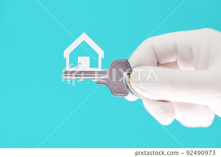 Close-up of a hand in a white glove holding a new metal key on a bright turquoise background. The symbol of the house. Leasing and mortgage concept Close-up of a hand in a white glove holding a new metal key on a bright turquoise background. The symbol of the house. Leasing and mortgage concept 92490973