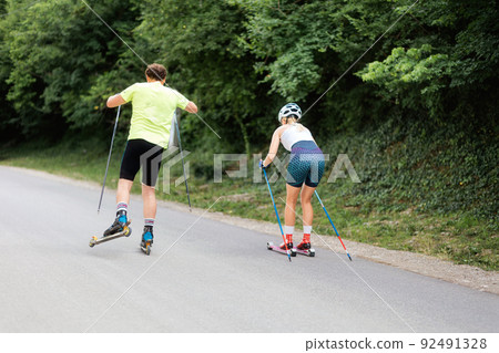 Athletic woman and man together training on the roller ski. Back view. Concept of competition, biathlon, and summer workout 92491328