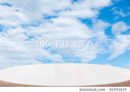A white marble oval pedestal or table surface on a bright blue cloudy sky background. Copy space. The concept of a product demonstration template 92491635