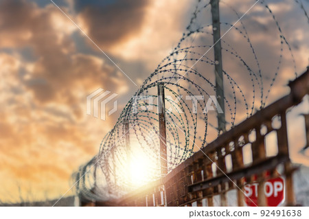 Immigration. A metal fence with barbed wire under tension. Cloudy sunset sky on the background. The concept of border protection, prison and hope 92491638
