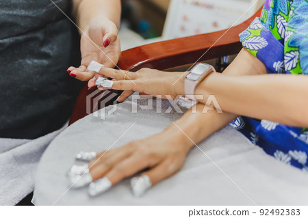 Woman in nail salon receiving a manicure by a beautician with cotton wool. Woman in nail salon receiving a manicure by a beautician with cotton wool. 92492383