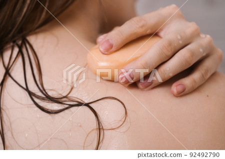 Closeup of female back with her hand on the shoulder with a bar of natural soap 92492790