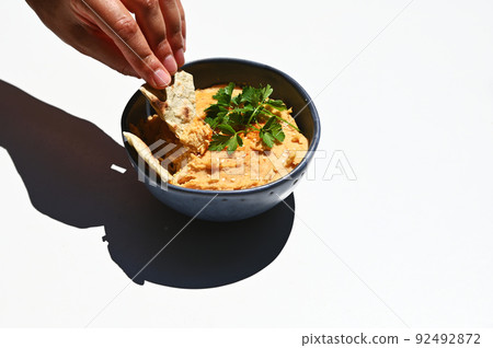 Close-up of human hand dipping pita bread into topped chickpea hummus, isolated on white background white Copy ad space Close-up of human hand dipping pita bread into topped chickpea hummus, isolated on white background white Copy ad space 92492872