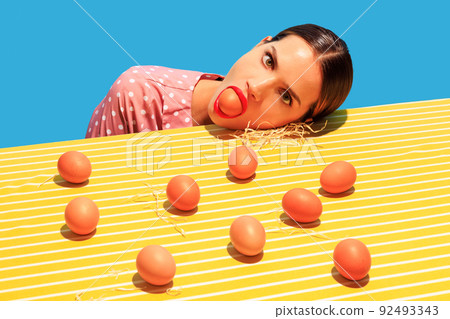Creative funny image of young woman and eggs on bright yellow tablecloth isolated on blue background. Household 92493343
