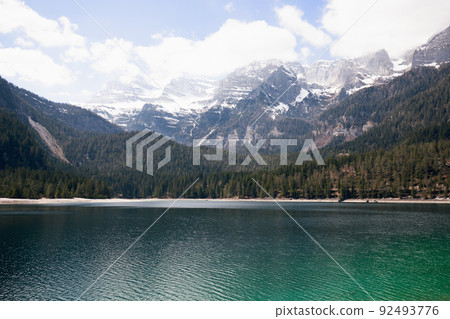 Aerial panoramic view of emerald water of a high-alpine Tovel lake surrounded by wooded and snowy 92493776