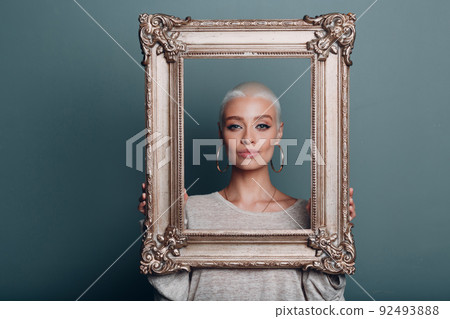 Museum restoration recovery renewal picture frame for painting art. Millenial young woman with short blonde hair holds gilded picture frame. 92493888