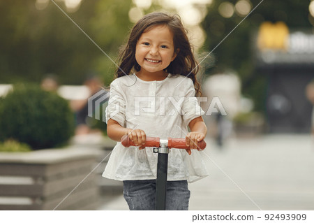 Child on kick scooter in park. Kids learn to skate roller board. Little girl skating on sunny summer day. Child on kick scooter in park. Kids learn to skate roller board. Little girl skating on sunny summer day. 92493909