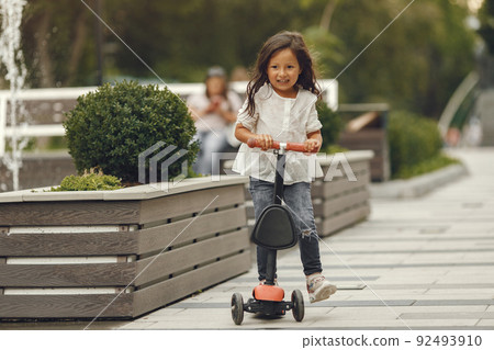 Child on kick scooter in park. Kids learn to skate roller board. Little girl skating on sunny summer day. Child on kick scooter in park. Kids learn to skate roller board. Little girl skating on sunny summer day. 92493910