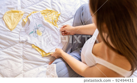 Pregnant woman baby clothes. Beautiful pregnancy mother with yellow baby clothes. Pregnant woman hugging belly and packing maternity hospital bag. Concept maternity, pregnancy, childbirth. 92494431
