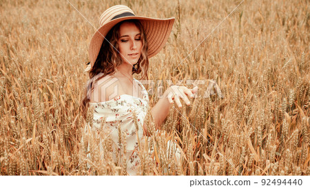 Girl wheat field summer. Happy young woman in sun hat in summer wheat field at sunset. Nature, summer holidays, vacation and people concept. 92494440