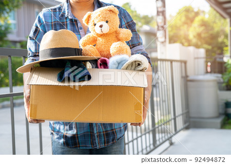 Holding clothing donation box with used clothes and doll at home to support help for poor people in the world. 92494872