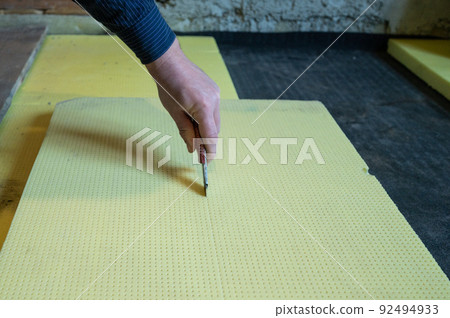 The master cuts expanded polystyrene on a floor, installation and warming of a floor in a room. The master cuts expanded polystyrene on a floor, installation and warming of a floor in a room. 92494933
