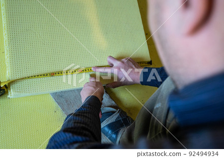 The master measures the length of expanded polystyrene on the floor, installation and insulation of the floor in the room. The master measures the length of expanded polystyrene on the floor, installation and insulation of the floor in the room. 92494934