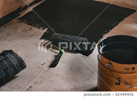 Applying hot resin to the floor for waterproofing, roller and bucket of resin. 92494956