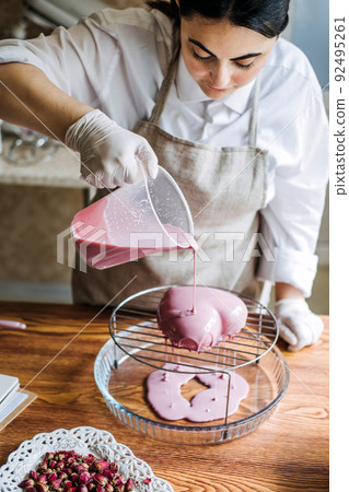 Mousse heart shape pink cake in hand of Asian Arabic woman pastry chef. Mirror Glaze Cake. Process Mousse heart shape pink cake in hand of Asian Arabic woman pastry chef. Mirror Glaze Cake. Process 92495261