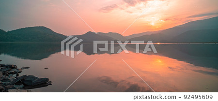 Panorama scenic of mountain lake with perfect reflection at sunrise. beautiful mountain range landscape with pink pastel sky with hills on background and reflected in water. Nature lake landscape Panorama scenic of mountain lake with perfect reflection at sunrise. beautiful mountain range landscape with pink pastel sky with hills on background and reflected in water. Nature lake landscape 92495609