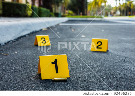 A group of yellow crime scene evidence markers on the street after a gun shooting brass bullet shell casing rifle A group of yellow crime scene evidence markers on the street after a gun shooting brass bullet shell casing rifle 92496285
