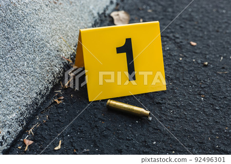 One yellow crime scene evidence marker on the street after a gun shooting brass bullet shell casing rifle One yellow crime scene evidence marker on the street after a gun shooting brass bullet shell casing rifle 92496301