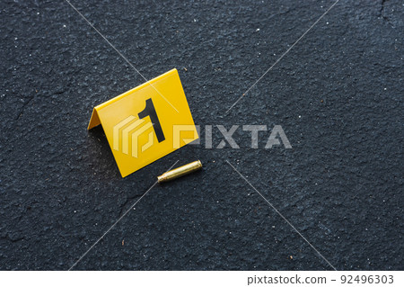 One yellow crime scene evidence marker on the street after a gun shooting brass bullet shell casing rifle 92496303