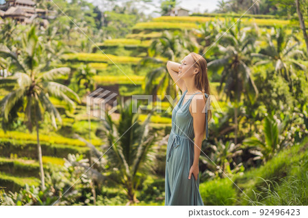 Beautiful young woman walk at typical Asian hillside with rice farming, mountain shape green cascade rice field terraces paddies. Ubud, Bali, Indonesia. Bali travel concept 92496423