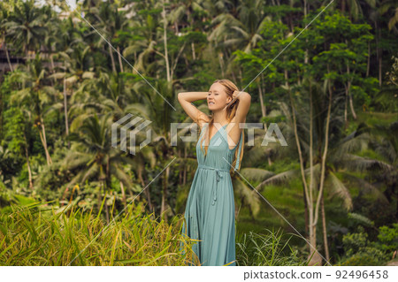 Beautiful young woman walk at typical Asian hillside with rice farming, mountain shape green cascade rice field terraces paddies. Ubud, Bali, Indonesia. Bali travel concept Beautiful young woman walk at typical Asian hillside with rice farming, mountain shape green cascade rice field terraces paddies. Ubud, Bali, Indonesia. Bali travel concept 92496458