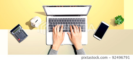 Woman using a laptop computer with a piggy bank Woman using a laptop computer with a piggy bank 92496791