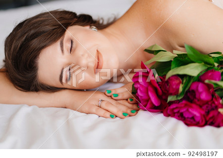 a gentle brunette woman in bed with a bouquet of peonies. morning of holiday. 92498197