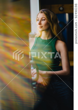 a young attractive blonde woman in a green top by the window. solar flare a young attractive blonde woman in a green top by the window. solar flare 92498198