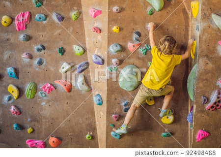 little boy climbing a rock wall in special boots. indoor 92498488