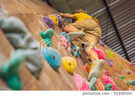 little boy climbing a rock wall in special boots. indoor little boy climbing a rock wall in special boots. indoor 92498504