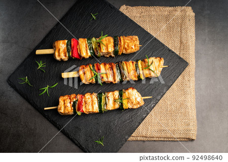 Chicken shish kebab with zucchini. Top view.Grilled pieces of chicken meat on skewers.Grilled chicken kebab with vegetables on a black background. Chicken shish kebab with zucchini. Top view.Grilled pieces of chicken meat on skewers.Grilled chicken kebab with vegetables on a black background. 92498640
