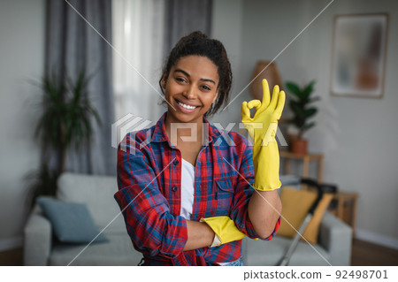 Glad millennial black lady in rubber gloves shows ok sign with hand in living room interior Glad millennial black lady in rubber gloves shows ok sign with hand in living room interior 92498701